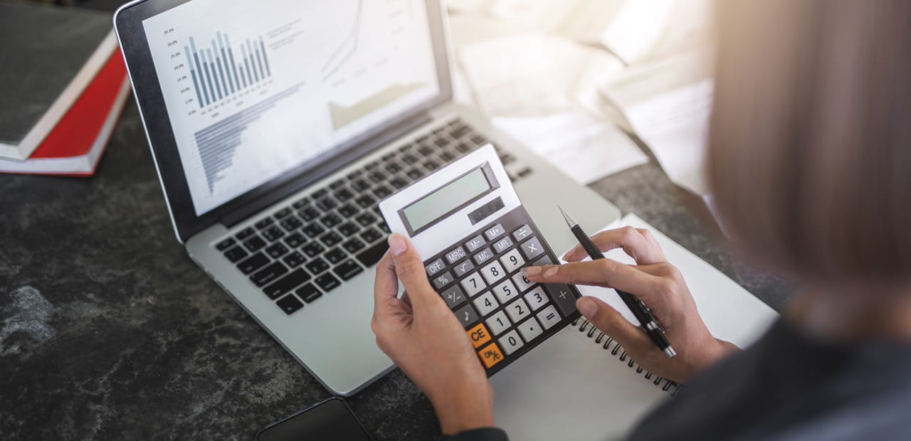 Woman's hands using a calculator while on her laptop computer.