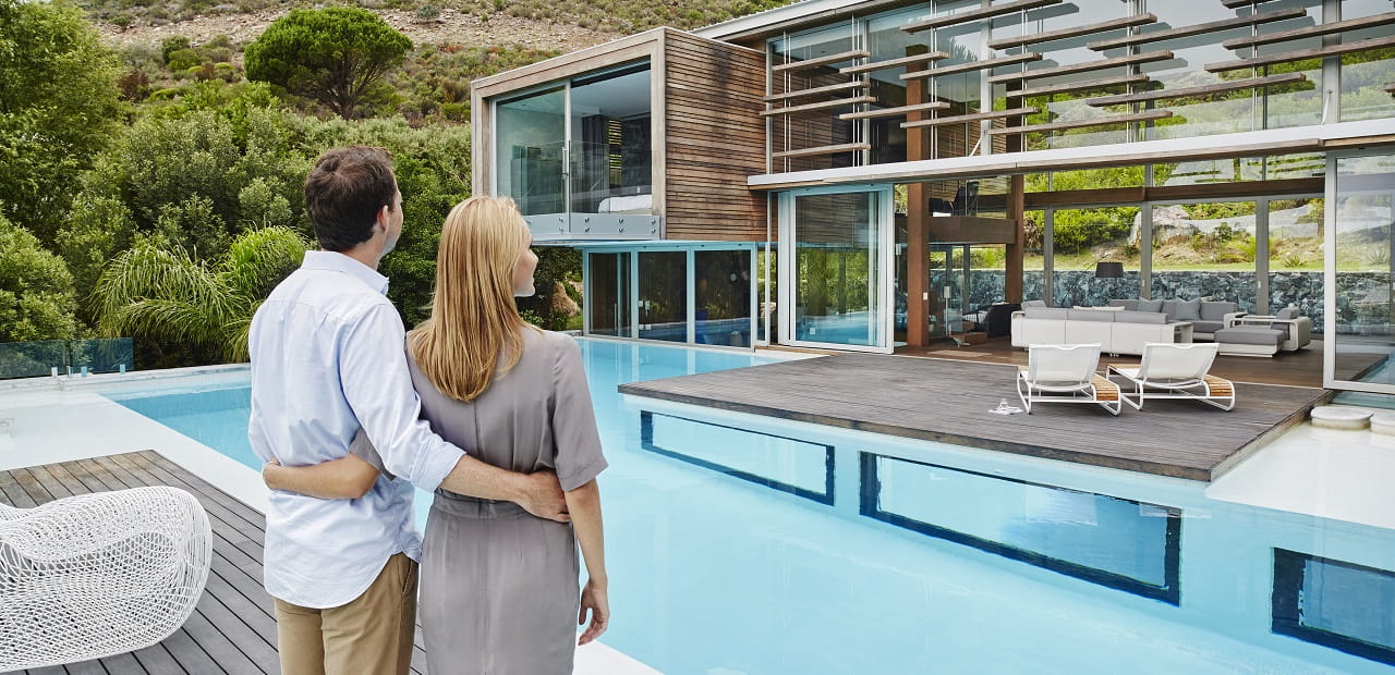 Couple standing behind their home looking at their pool and house.